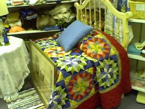 Using a for-sale head board, a packing box, and a for-sale bedspread in a thrift, consignment or resale shop